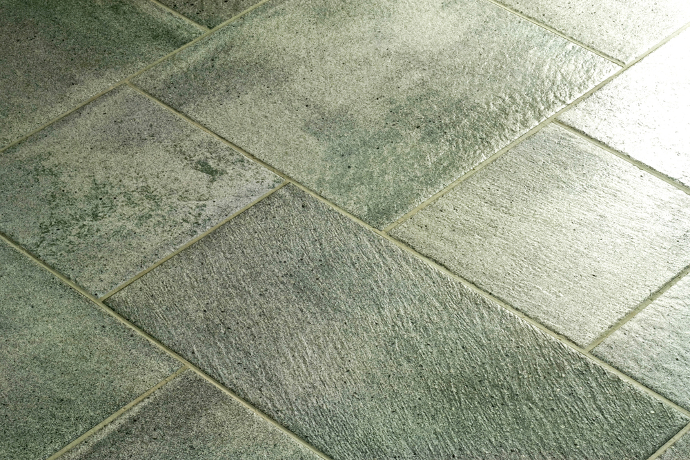Close-up view of a floor with large rectangular greenish-grey tiles arranged in a staggered pattern.